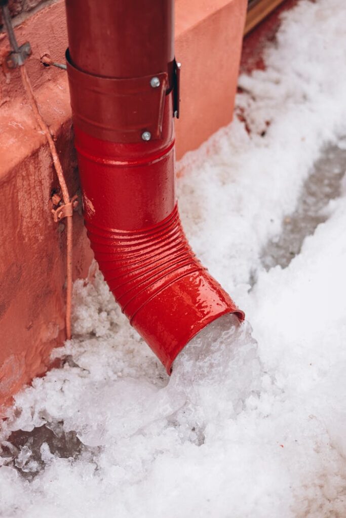 Close-up of a red drainpipe with snow melting around it, capturing a winter scene.