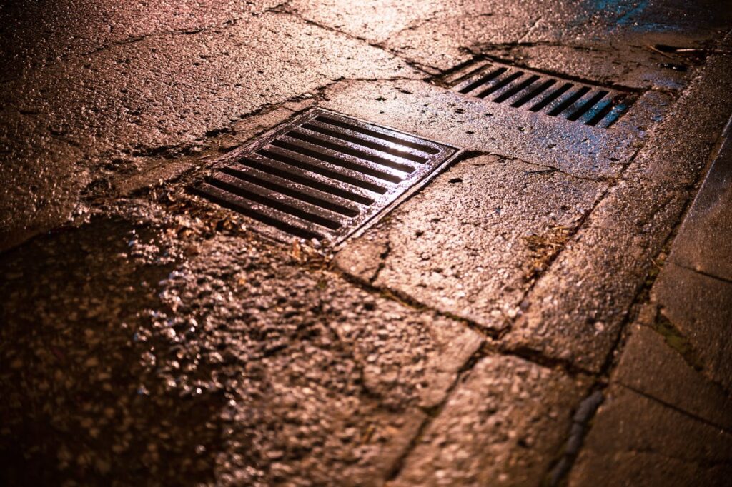 Nighttime shot of wet asphalt road with drainage grates reflecting light.