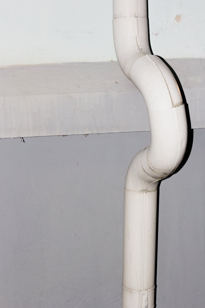 Vertical shot of a curved white drainage pipe against a concrete wall.